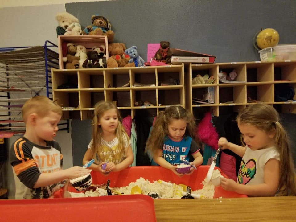 Four children playing with sensory bins in a classroom