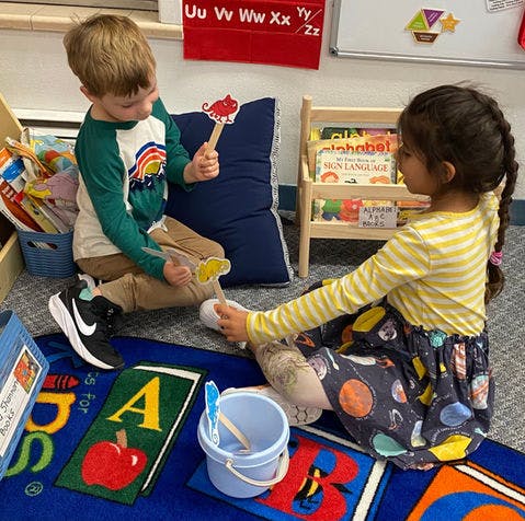 Two children playing with stick puppets in a classroom