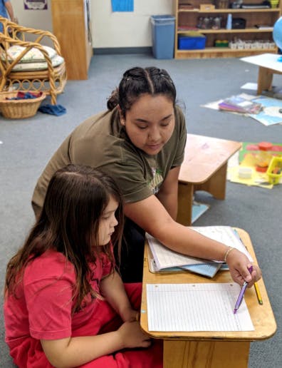 Person helping a child with schoolwork in a classroom