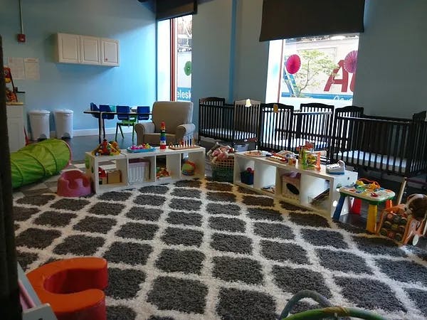 Daycare room with cribs, play tables, and a patterned rug