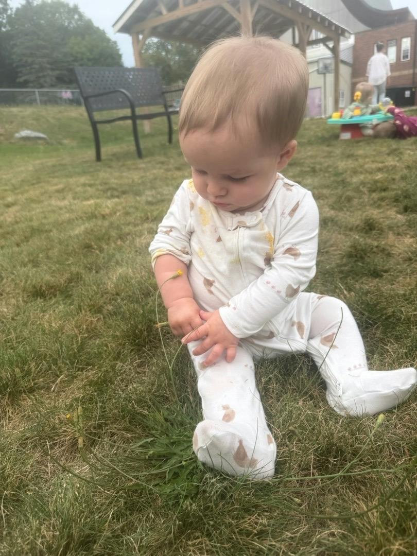 Child sitting on grass touching a small flower