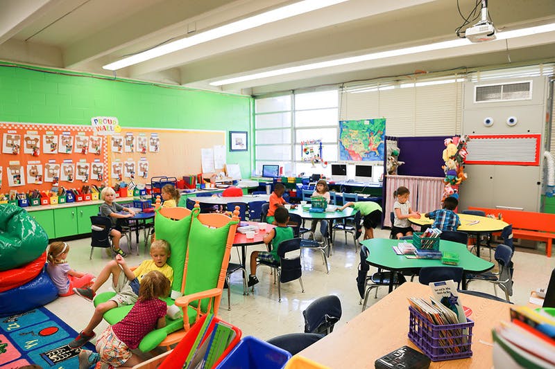 Children in a classroom sitting at tables and on the floor