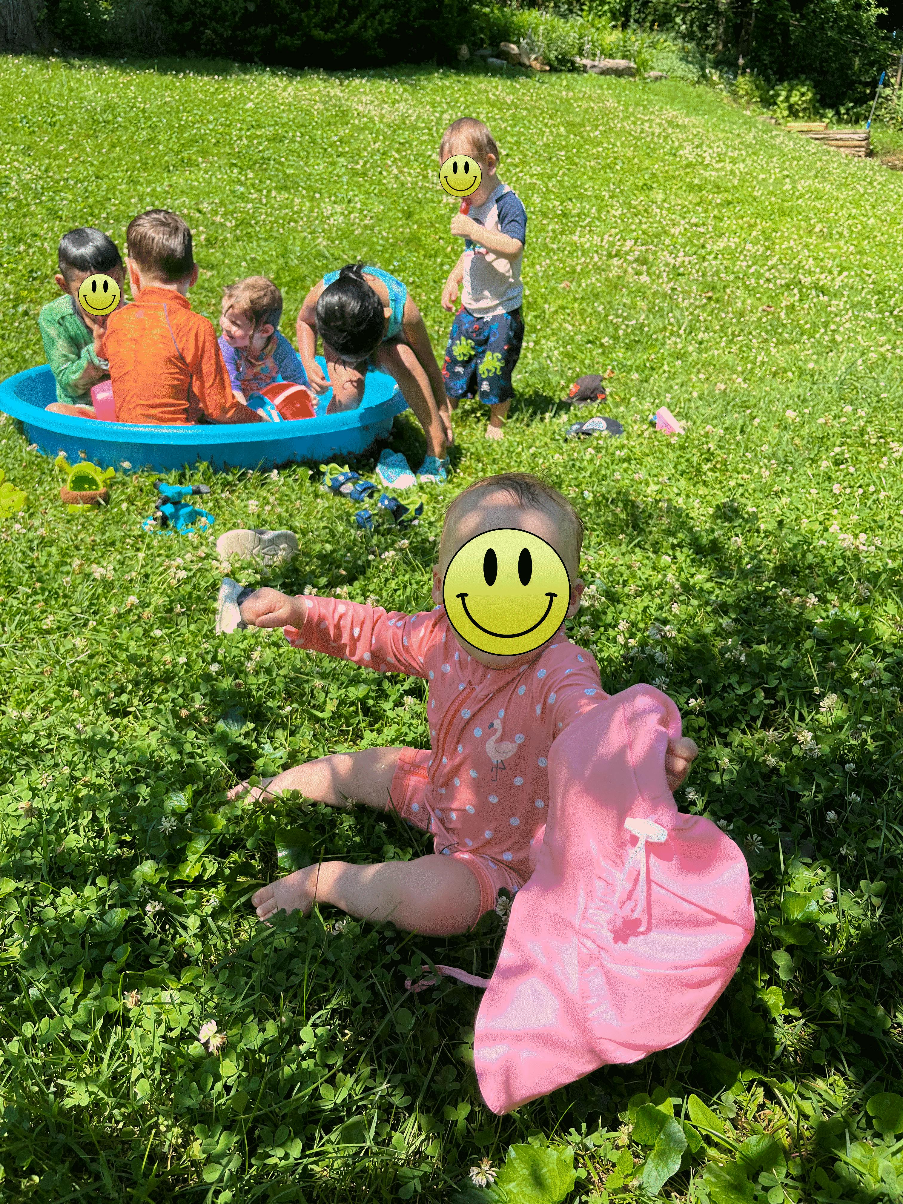 Group of children playing in a backyard paddling pool and on the grass