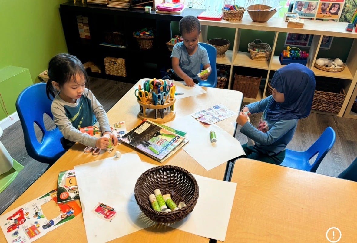 Three children working on a craft project at a table in a classroom