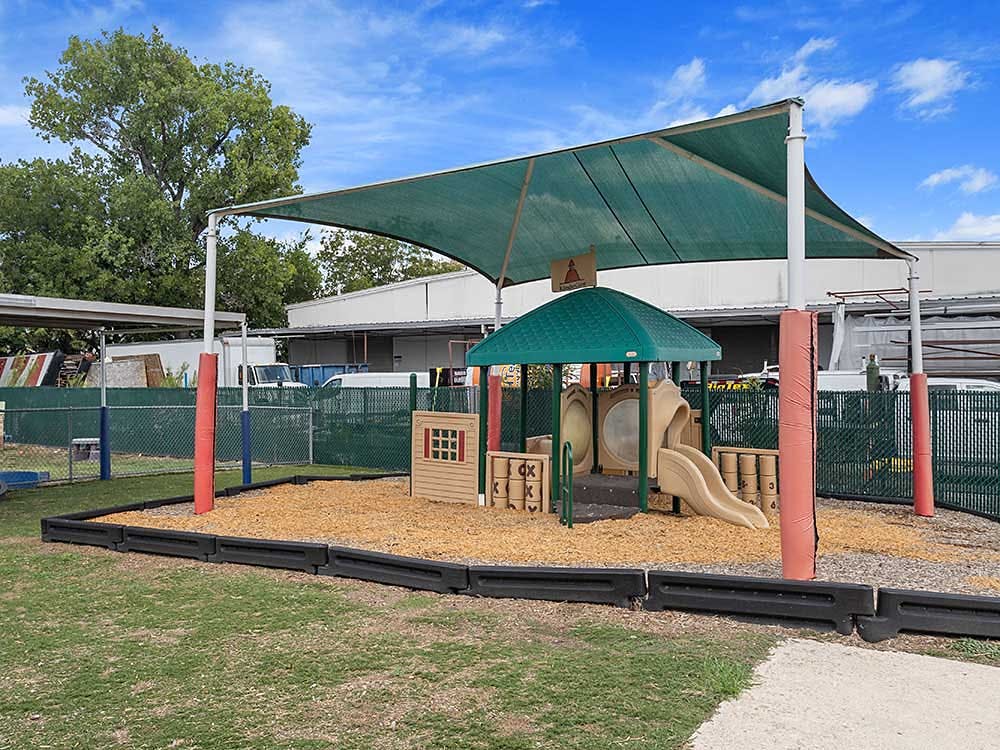 Playground with a small play structure and slide under a green shade