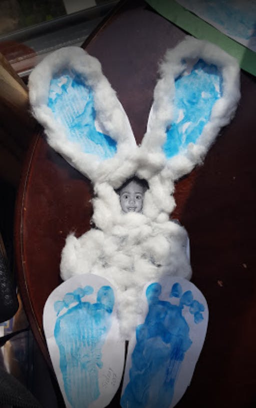 Child's face in a cotton bunny craft with blue footprints