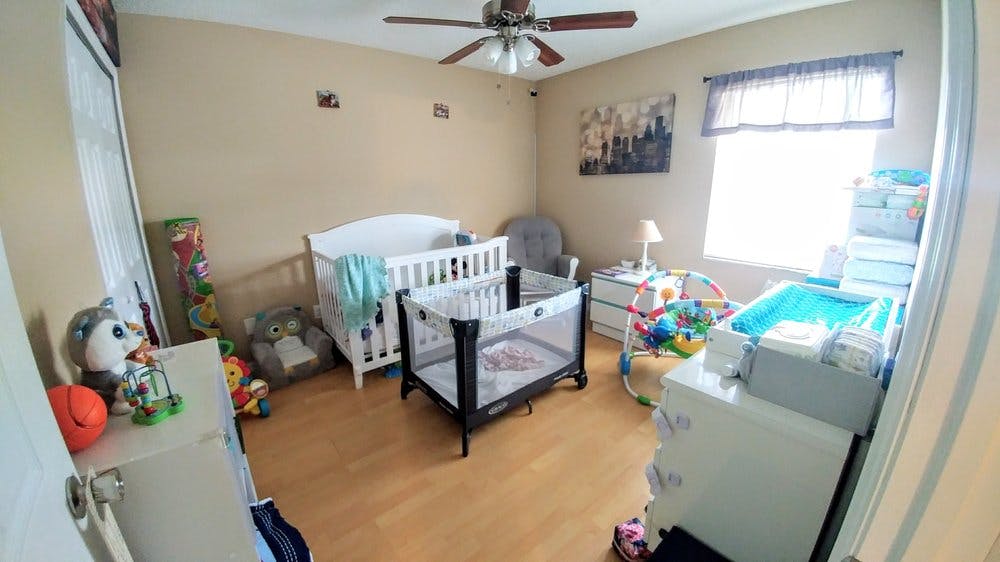 Nursery room with a white crib, playpen, changing table, and ceiling fan