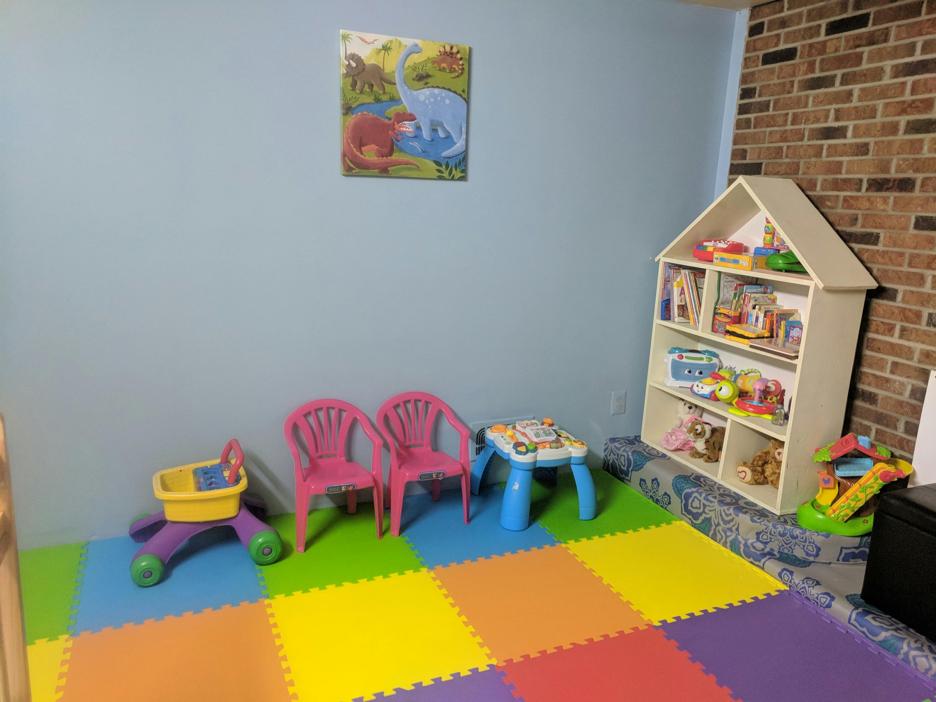 Playroom with colorful floor mats, small chairs, table, and toy shelf