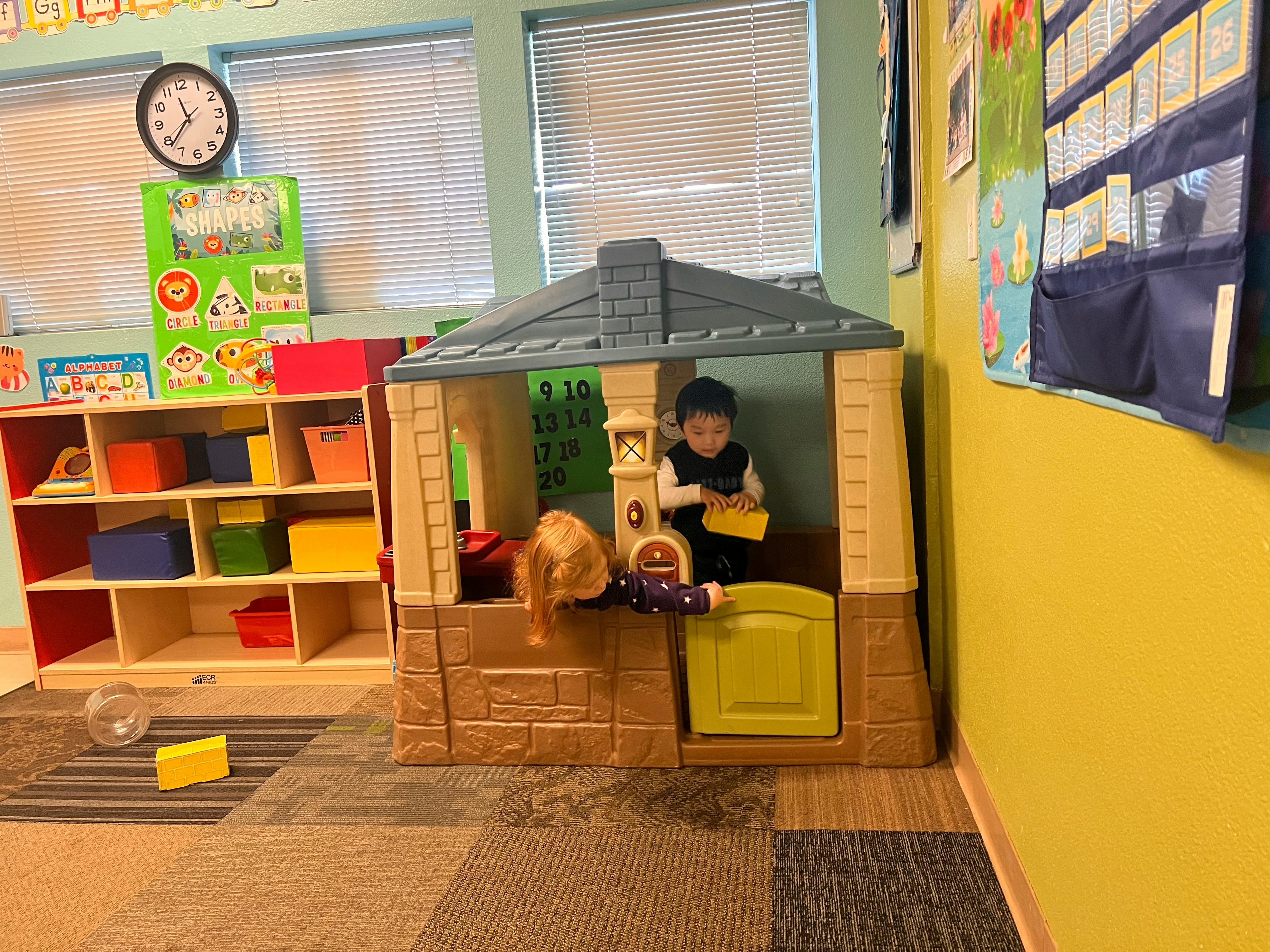 Child playing inside a toy house in a classroom
