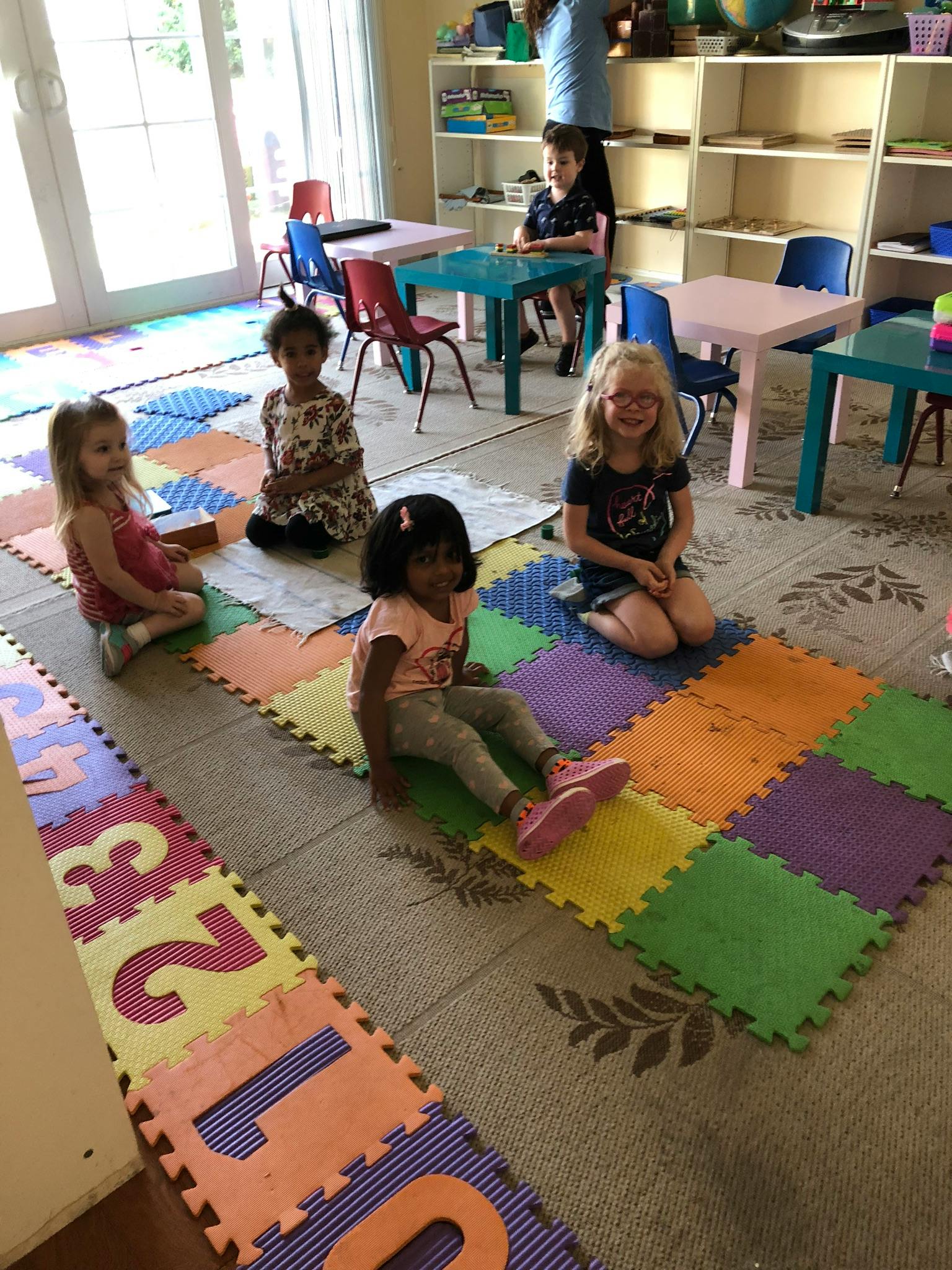 Four children sitting on colorful floor mats in a classroom