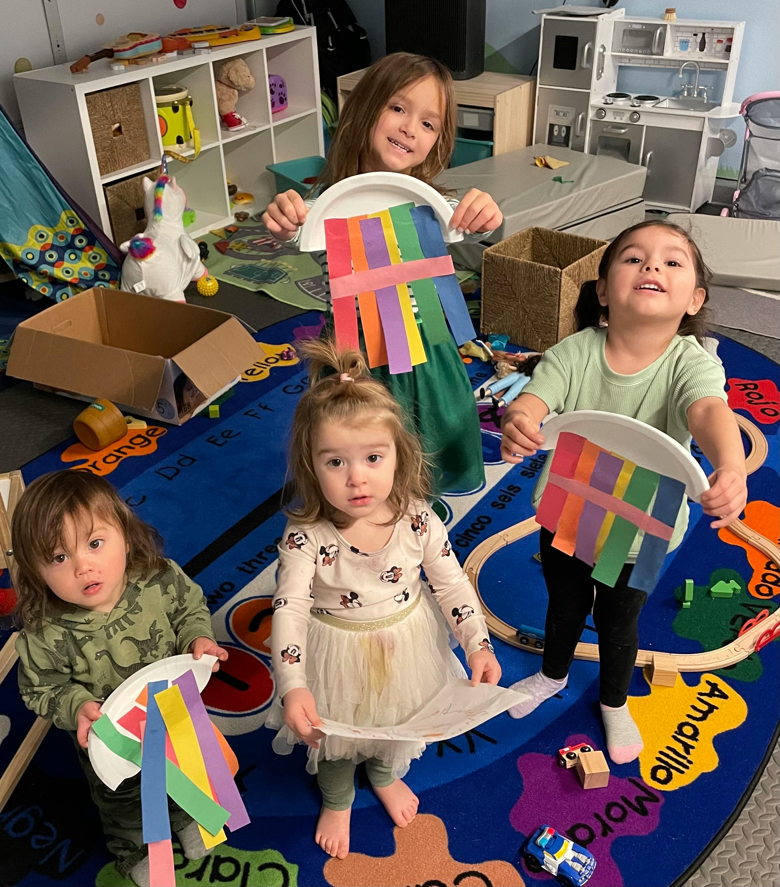 Four children holding paper plate crafts with colorful strips