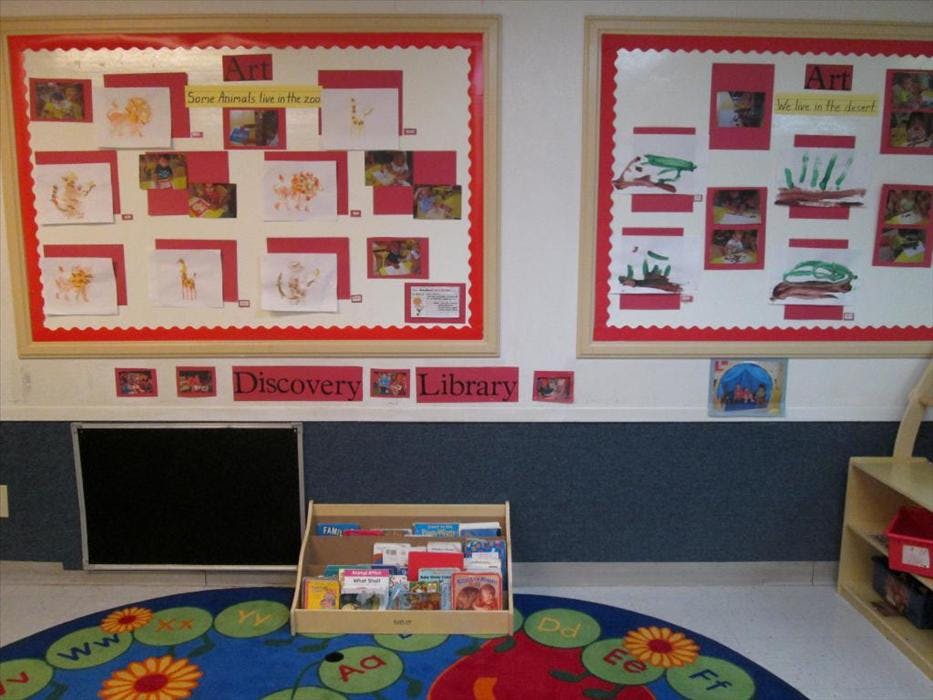 Classroom bulletin boards with children's artwork and a rug with alphabet letters