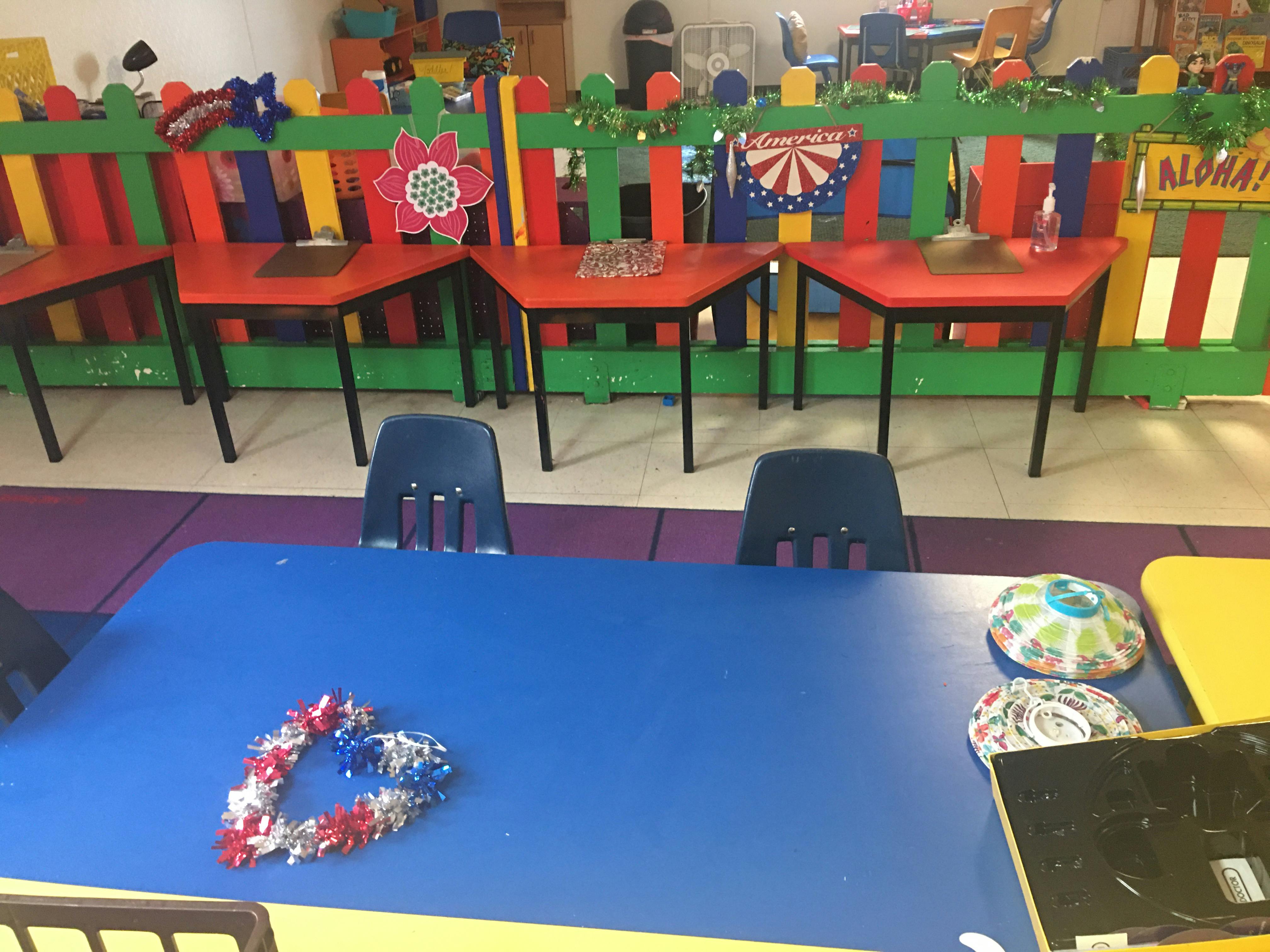 Classroom with blue table in foreground and red tables behind a colorful fence