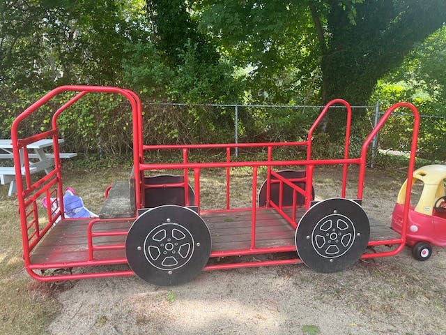 Red metal play structure shaped like a truck with a small toy car attached