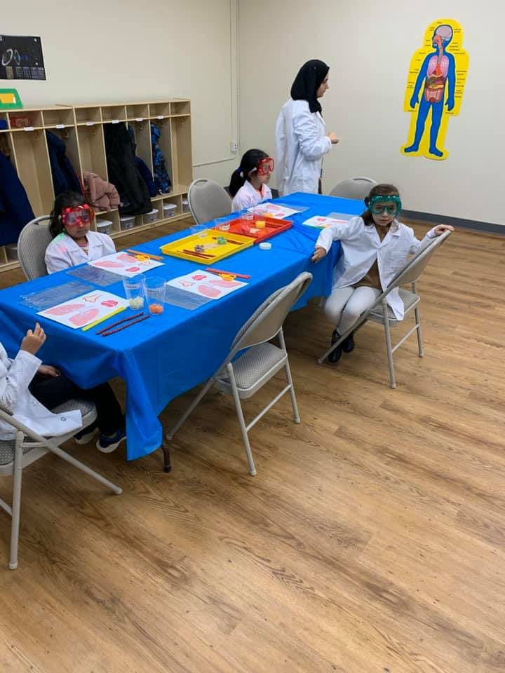 Children in lab coats and goggles at a table with science experiments