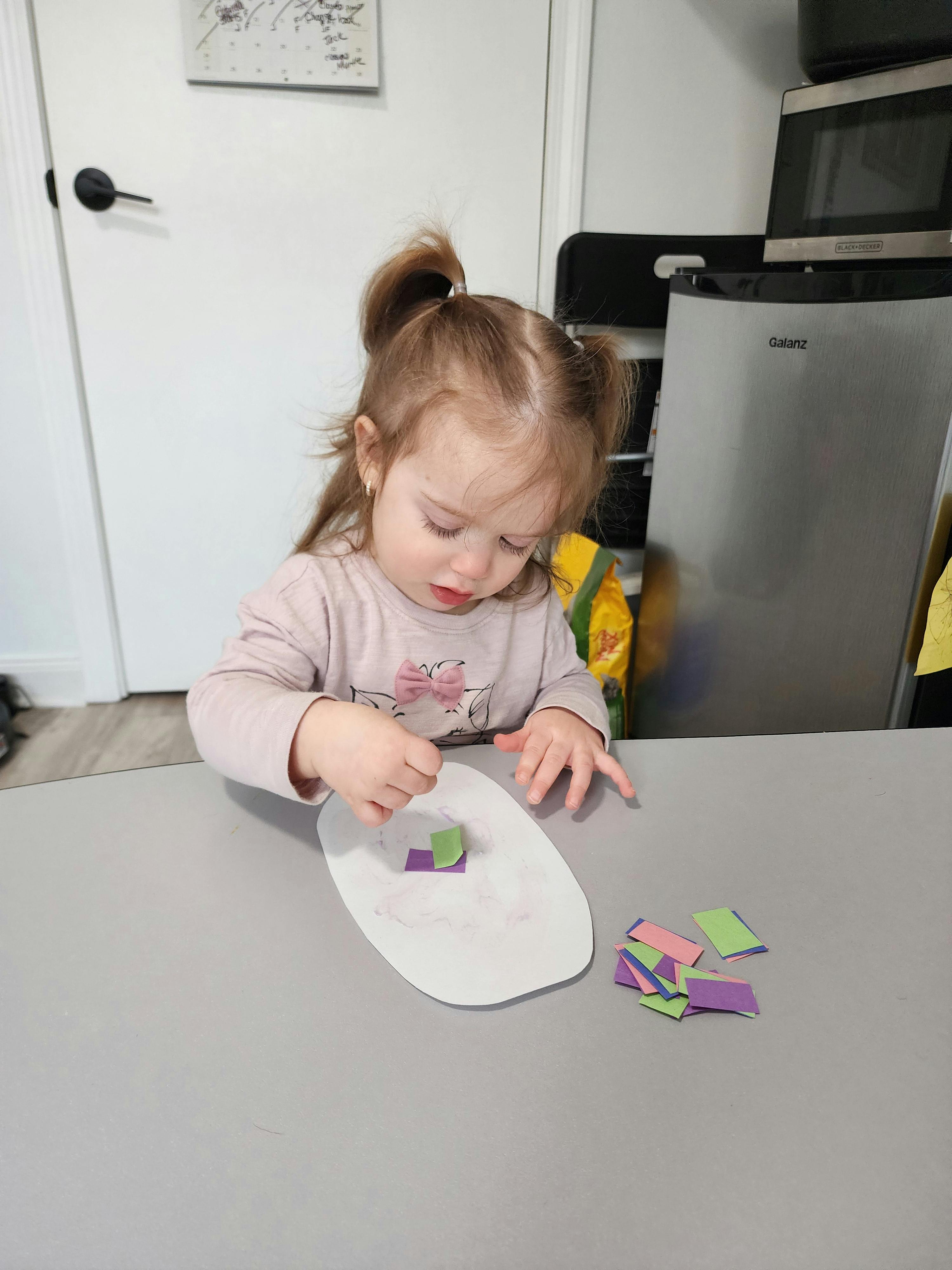 Child placing small paper pieces on a white surface
