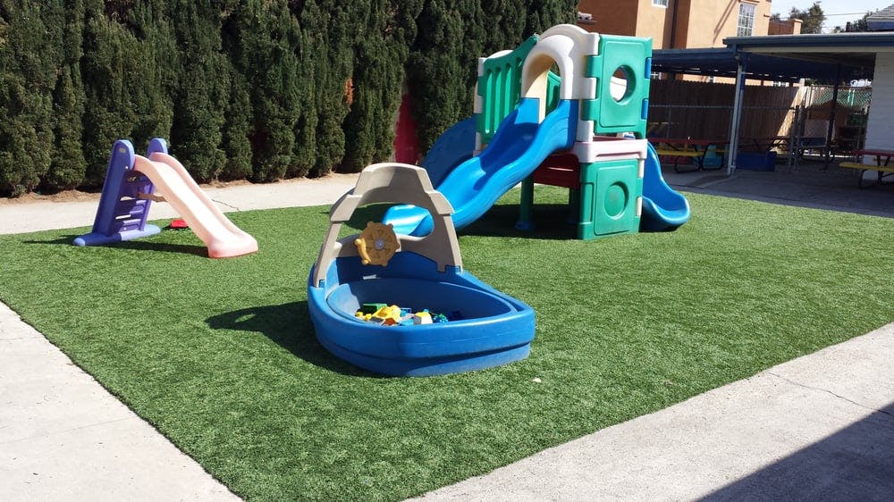 Playground with slides and a boat-shaped sandbox on artificial turf