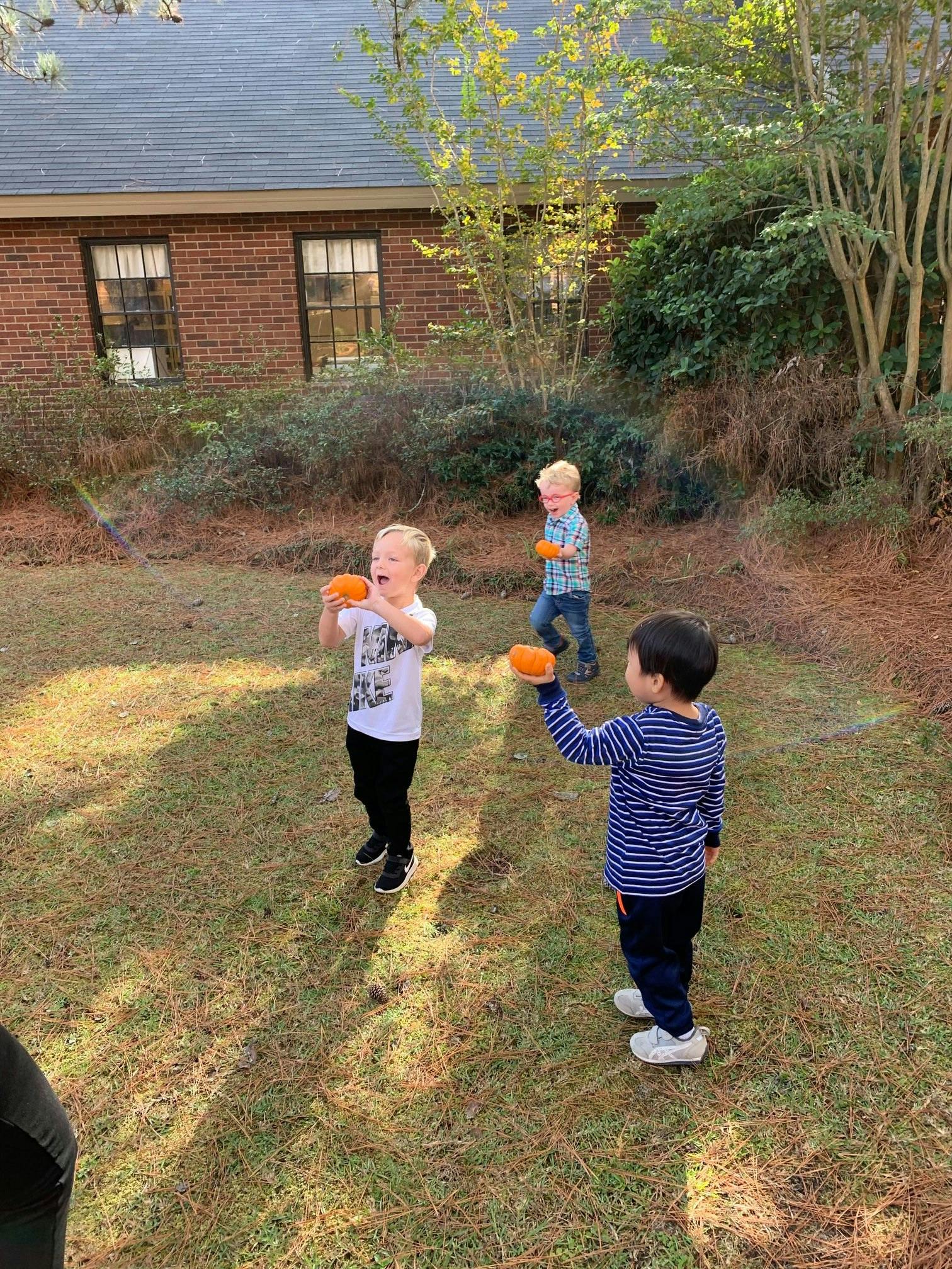 Three children playing with small orange objects outdoors