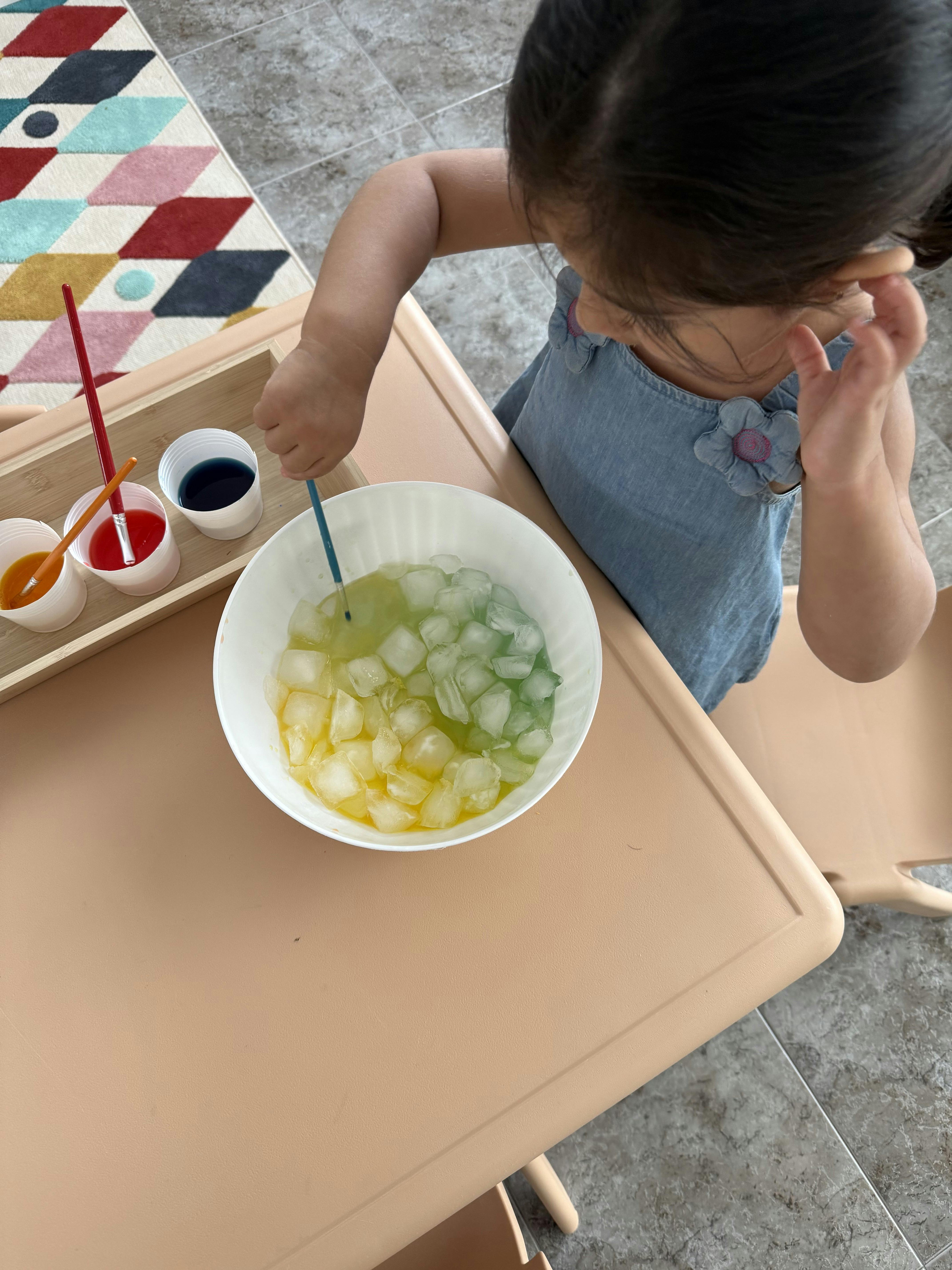 Child painting ice cubes in a bowl with a paintbrush