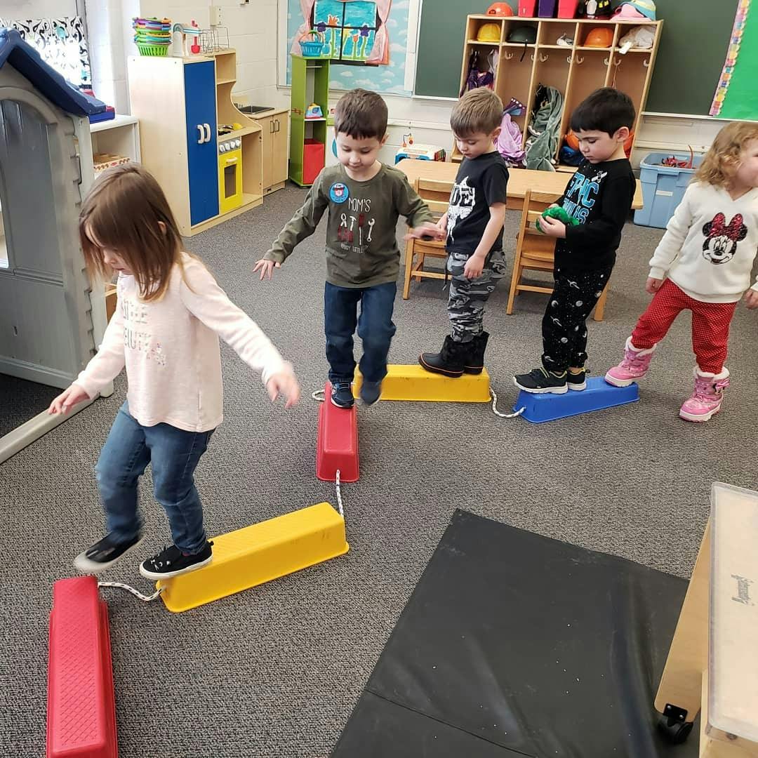Children walking on a balance beam in a classroom