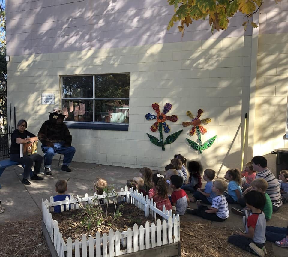 Two people sitting and playing drums for a group of children