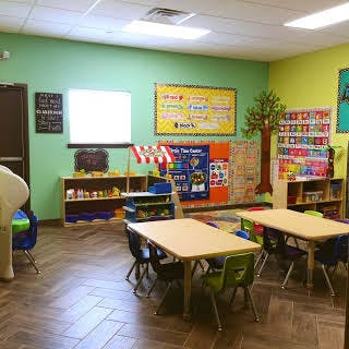 Classroom with small tables and chairs, shelves, and a projector screen