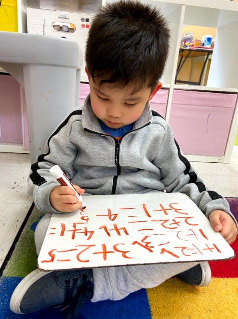 Child writing math problems on a whiteboard