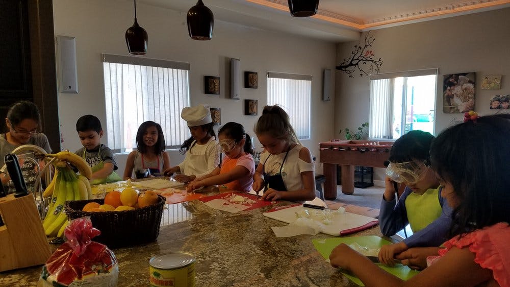 Children gathered around a counter, some wearing aprons and a chef's hat