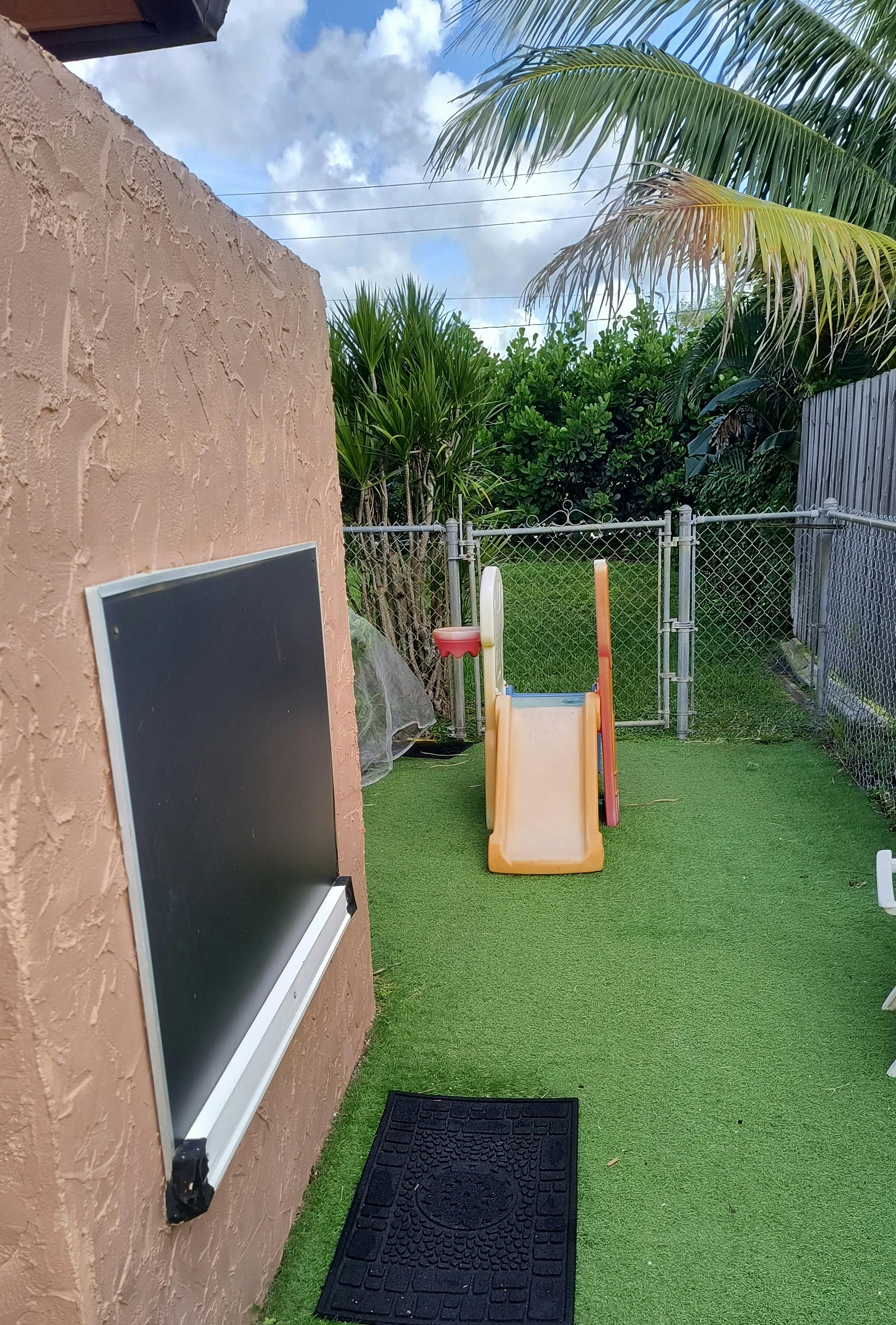 Small playground slide with a basketball hoop on an artificial grass yard
