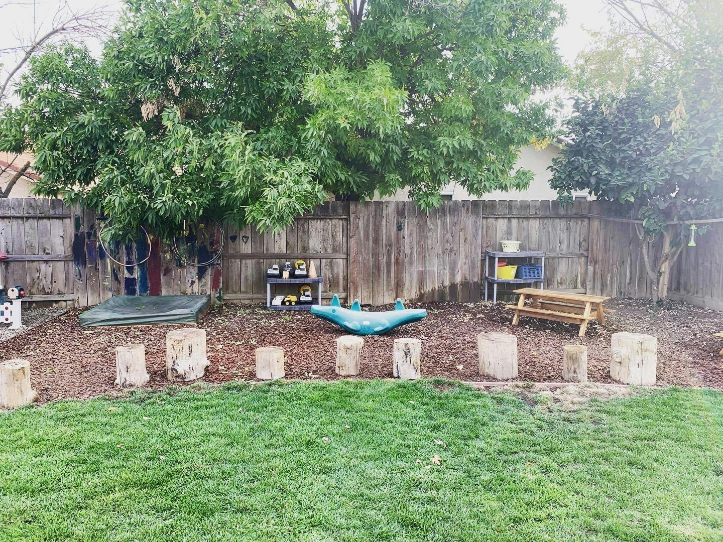 Outdoor play area with wooden fence, trees, and various play equipment