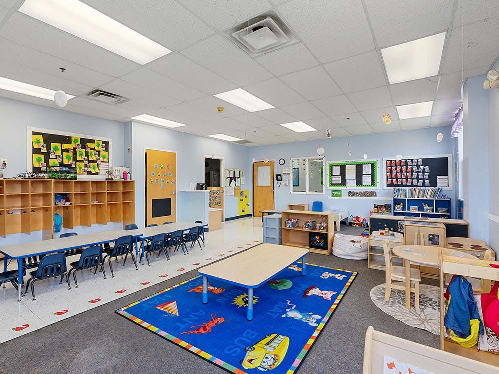Empty preschool classroom with small tables, chairs, and colorful rugs