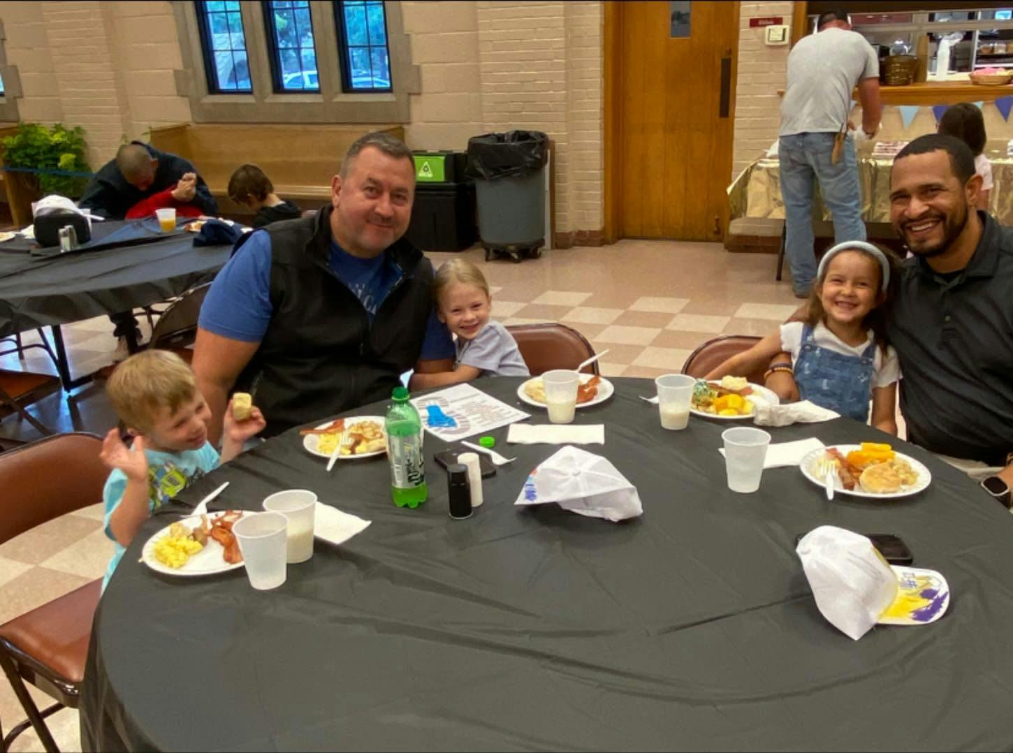 Two adults and two children seated at a round dining table with food