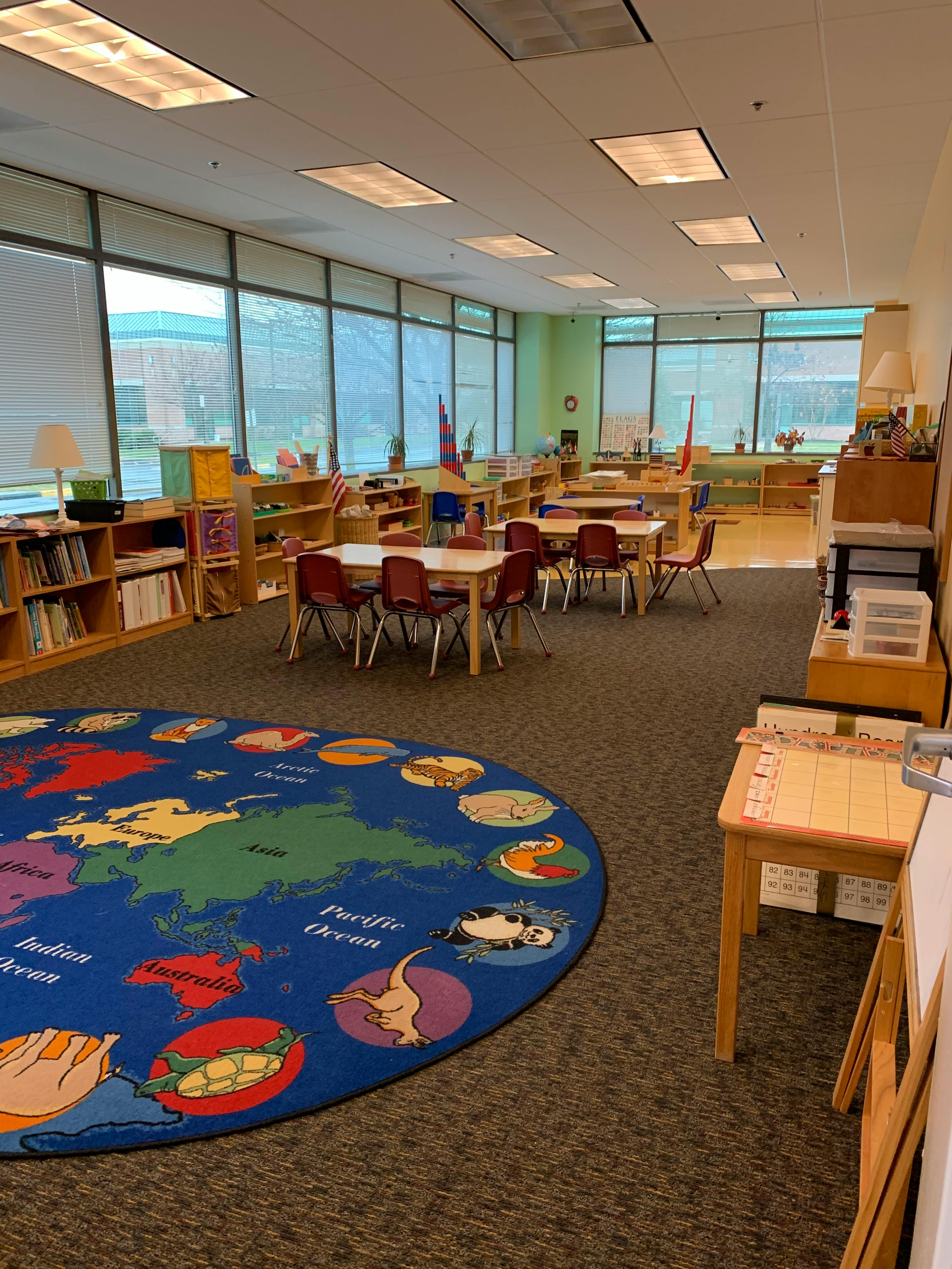 Classroom with tables and chairs, bookshelves, and a world map rug