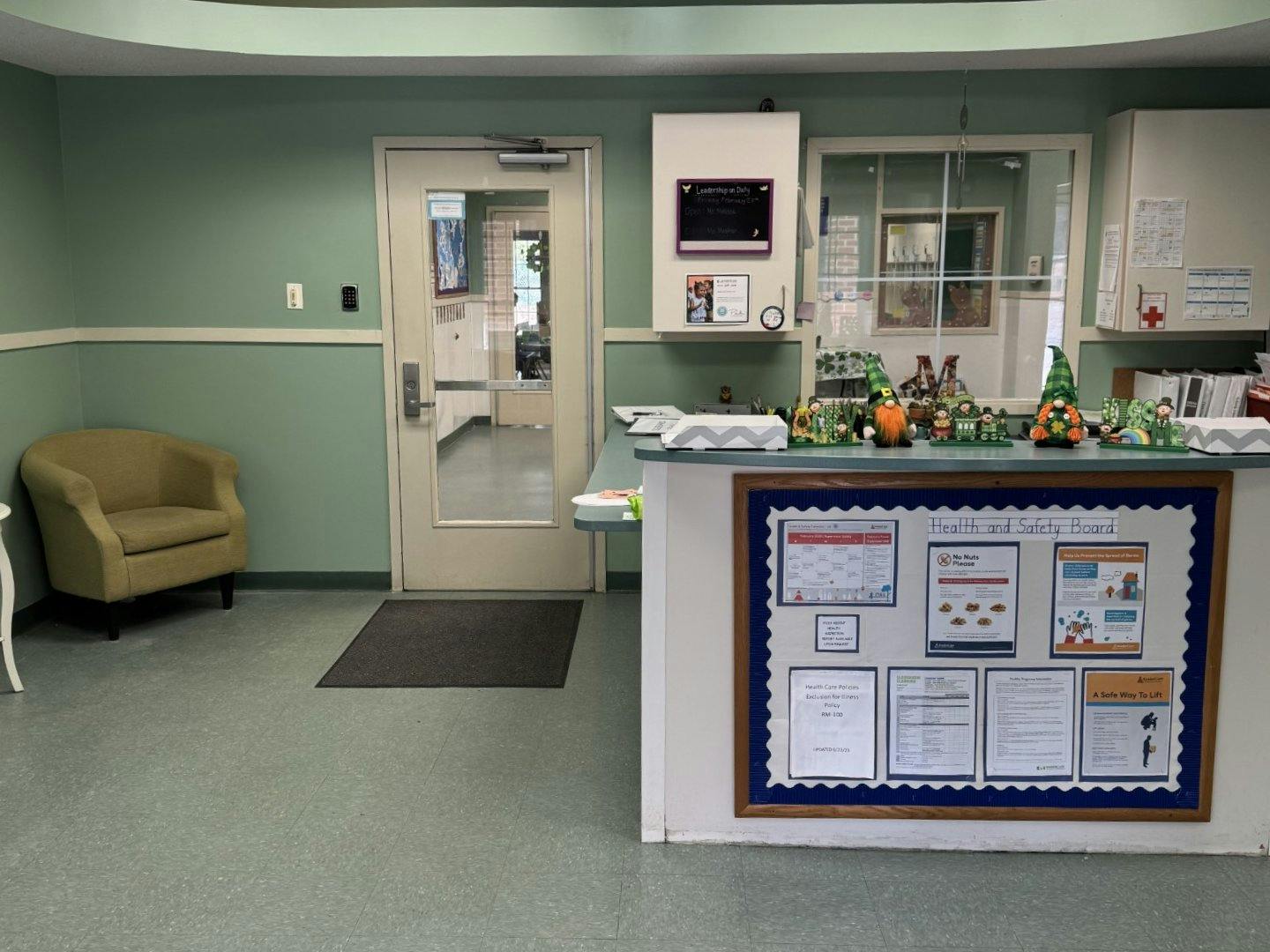 Reception area with a desk, health and safety board, door, and armchair