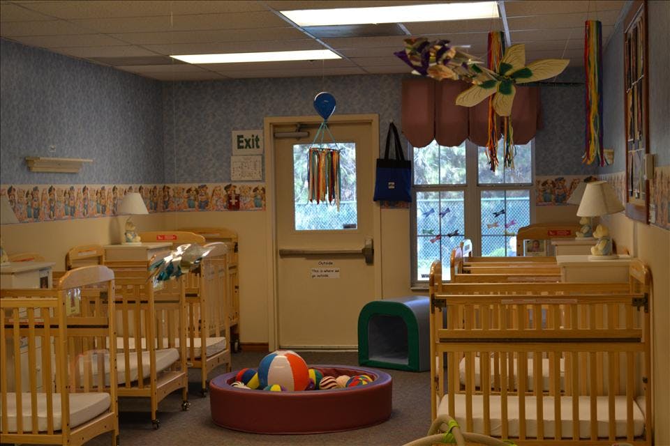 A room with multiple wooden cribs, a ball pit, and an exit sign over a door