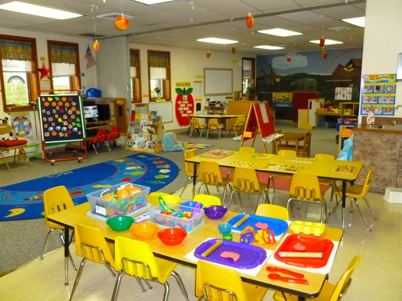 A colorful classroom with small tables and chairs, toys, and learning materials