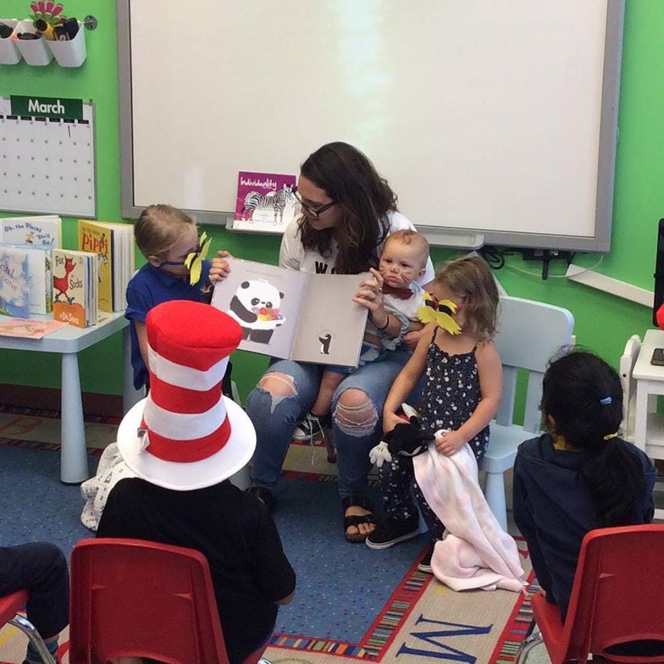 Person reading a book to children and a baby in a classroom