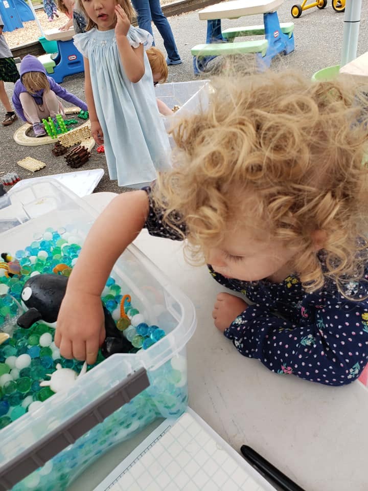 Child playing with water beads and toys in a clear bin