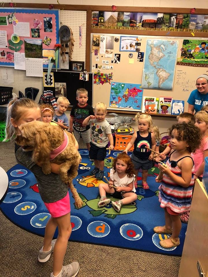 Teen holding a dog in a classroom with children around ten young children