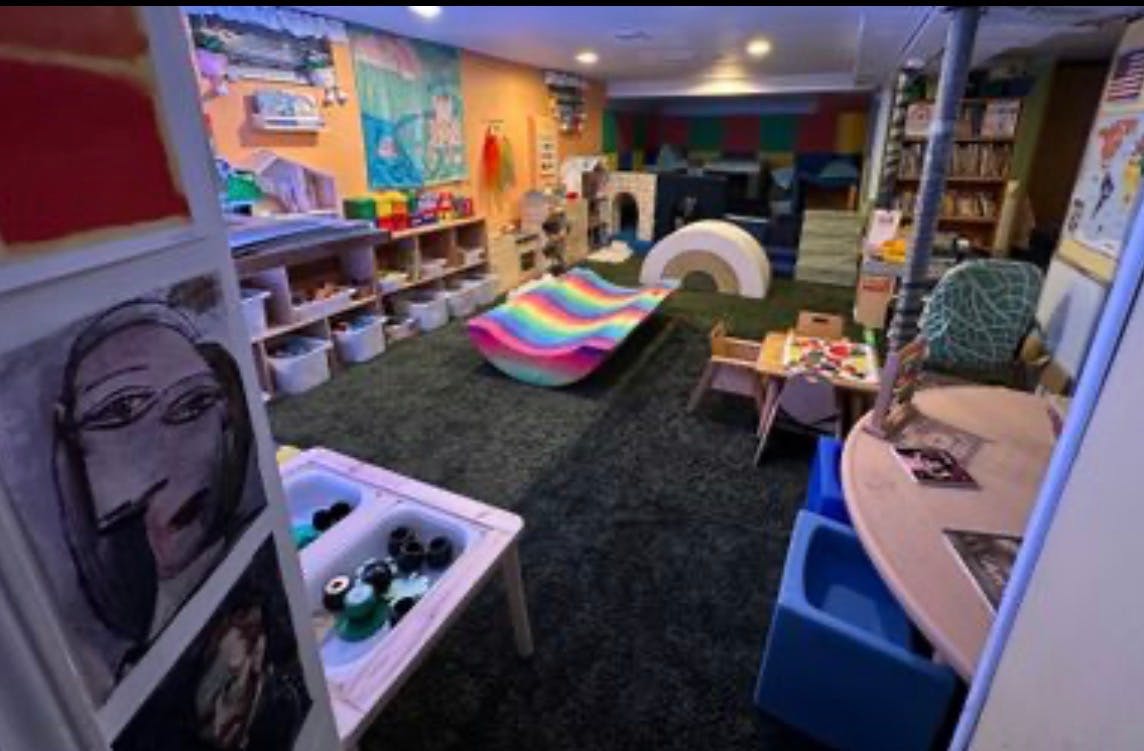 Playroom with artificial turf flooring, a rainbow rocker, and play furniture