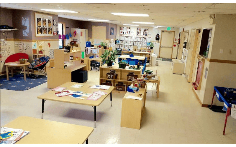 Empty classroom with small tables and chairs, shelves, and a blue rug with stars