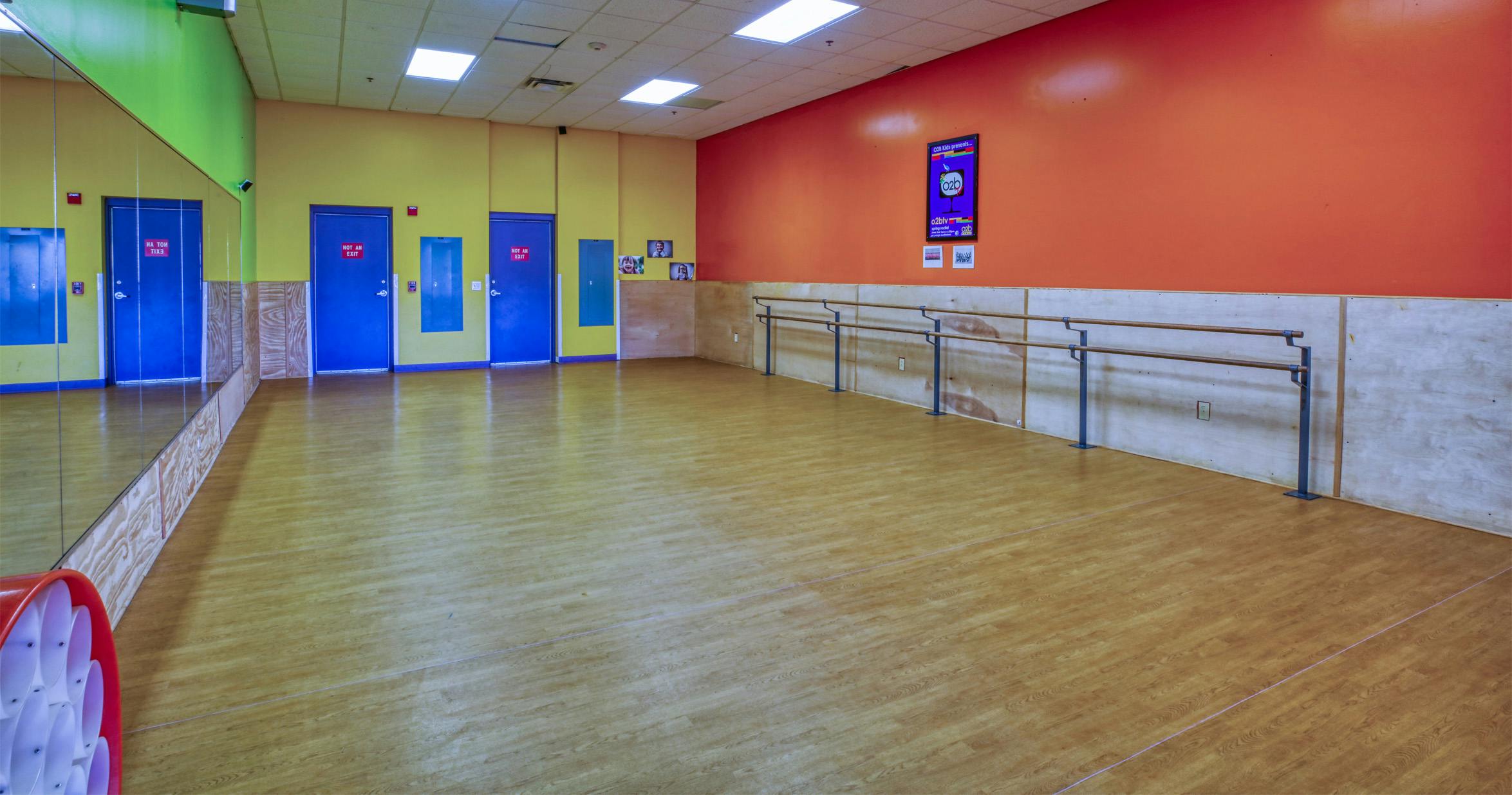 Empty dance studio with mirrors, three blue doors with "NOT AN EXIT" signs, and ballet barres