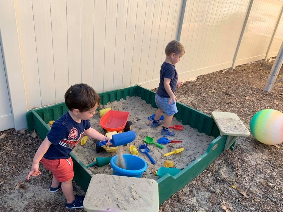 Two children playing in a sandbox with sand toys