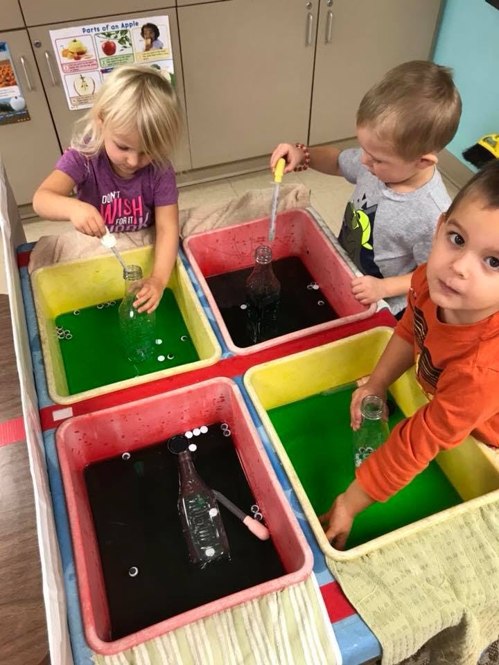 Three children playing with water and bottles in colorful bins