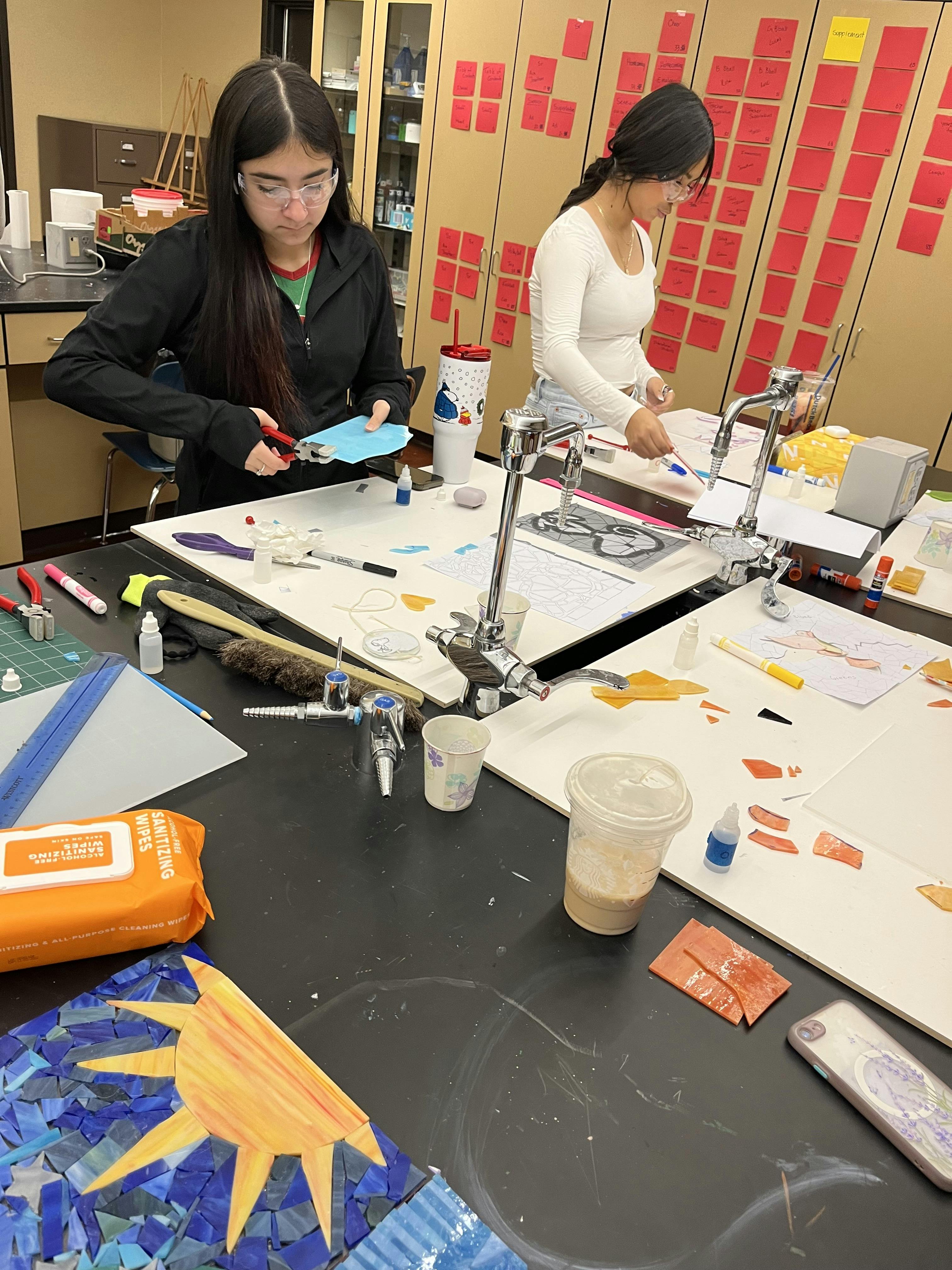 Two people working on crafts at a table, one cutting paper, the other gluing