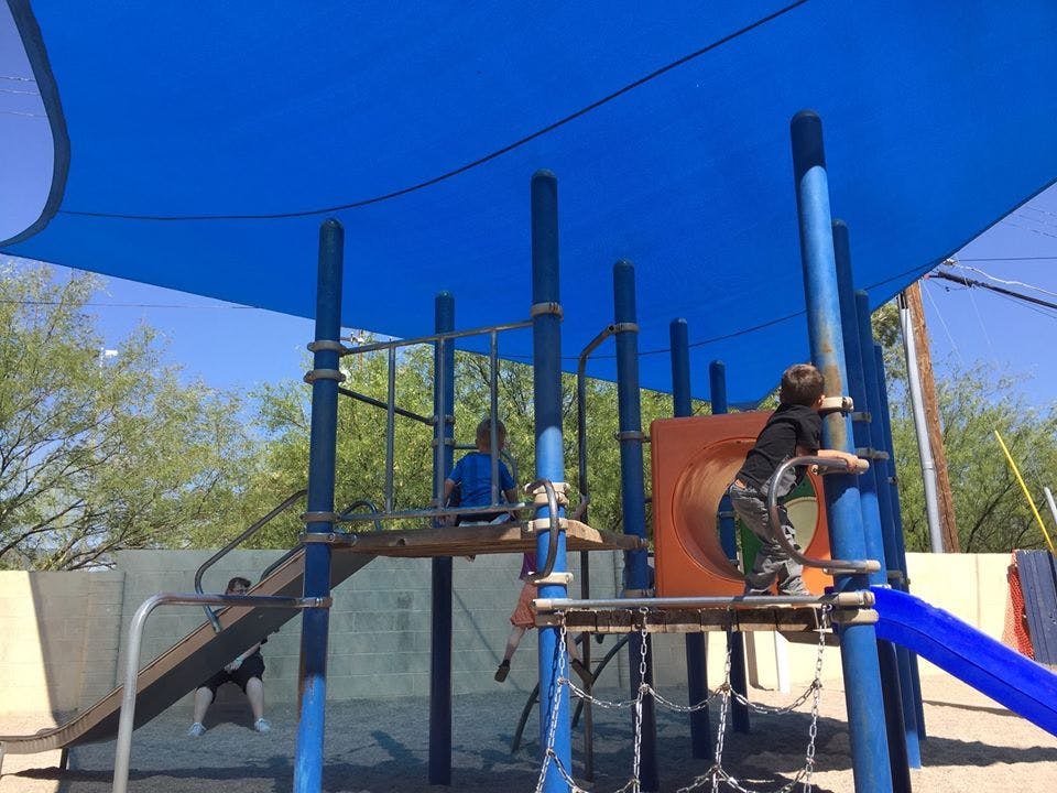Children playing on a playground structure under a blue shade canopy