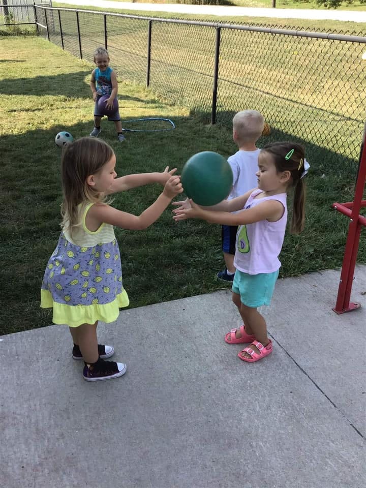 Two children playing with a green ball outdoors