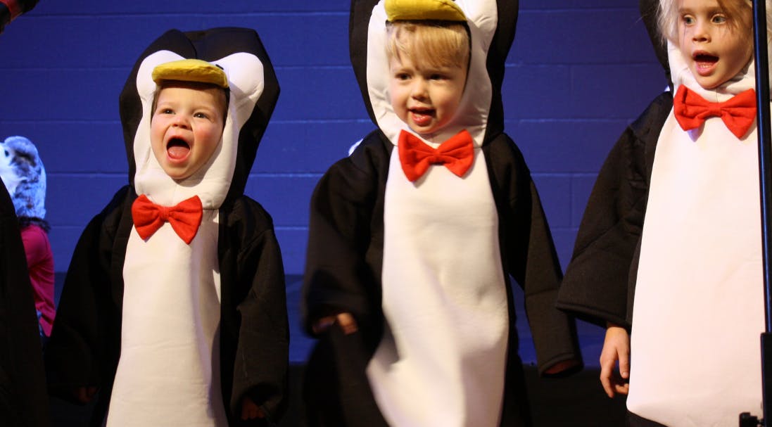 Children in penguin costumes with red bow ties