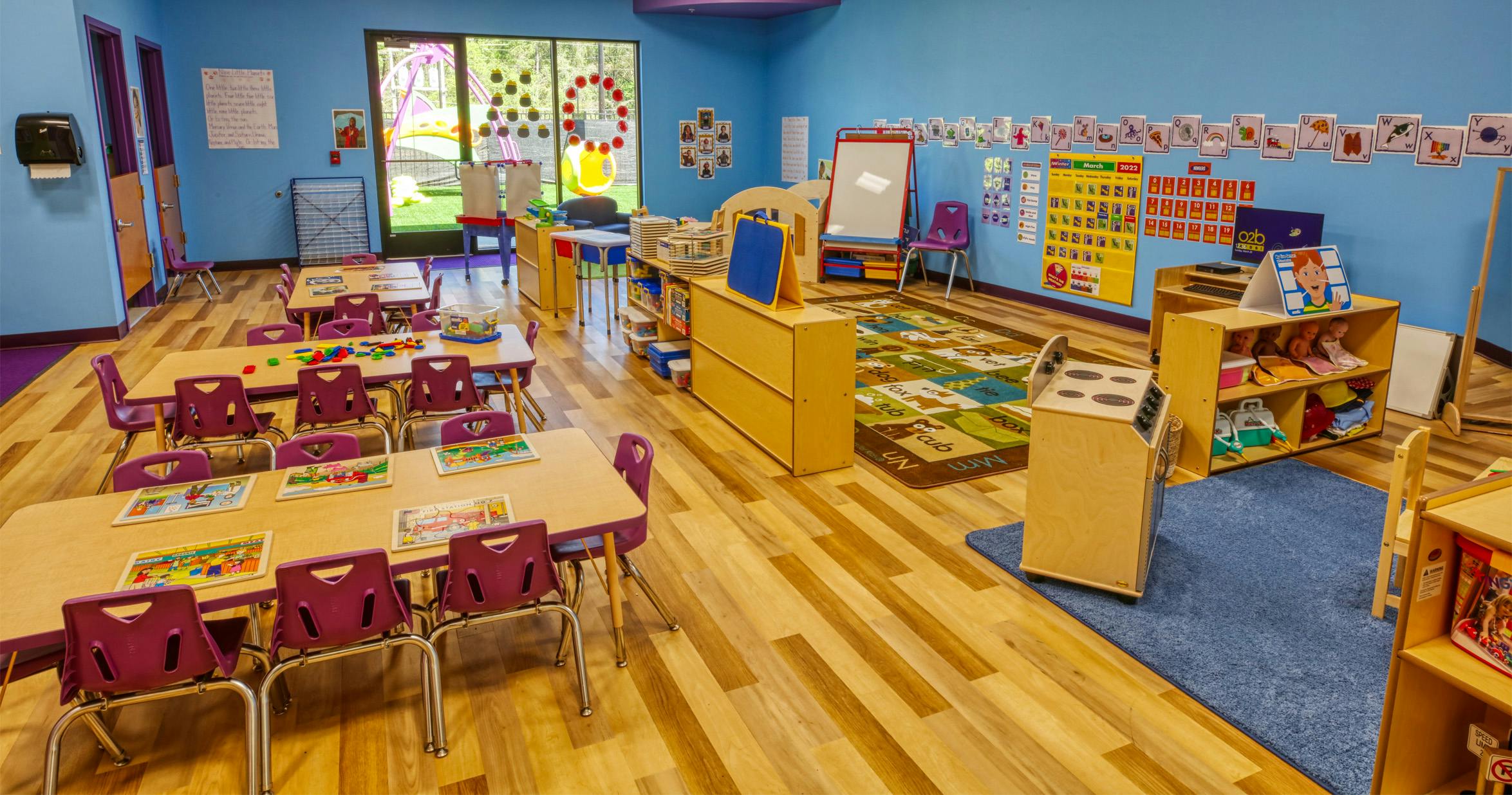 An empty colorful preschool classroom with tables, chairs, and toys