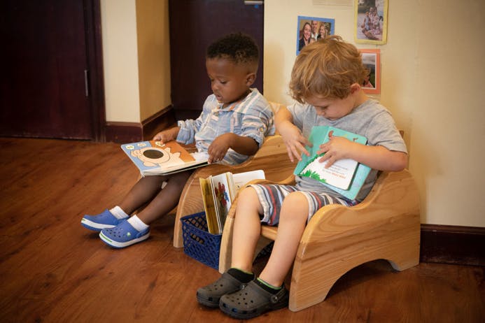 Two children sitting in chairs reading books